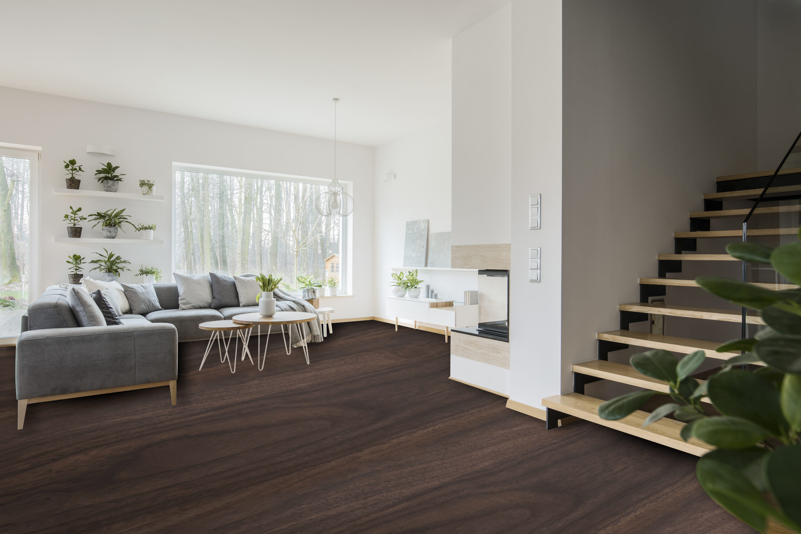 White living room interior with grey corner couch, fresh green plants, carpet on the floor and wooden stairs